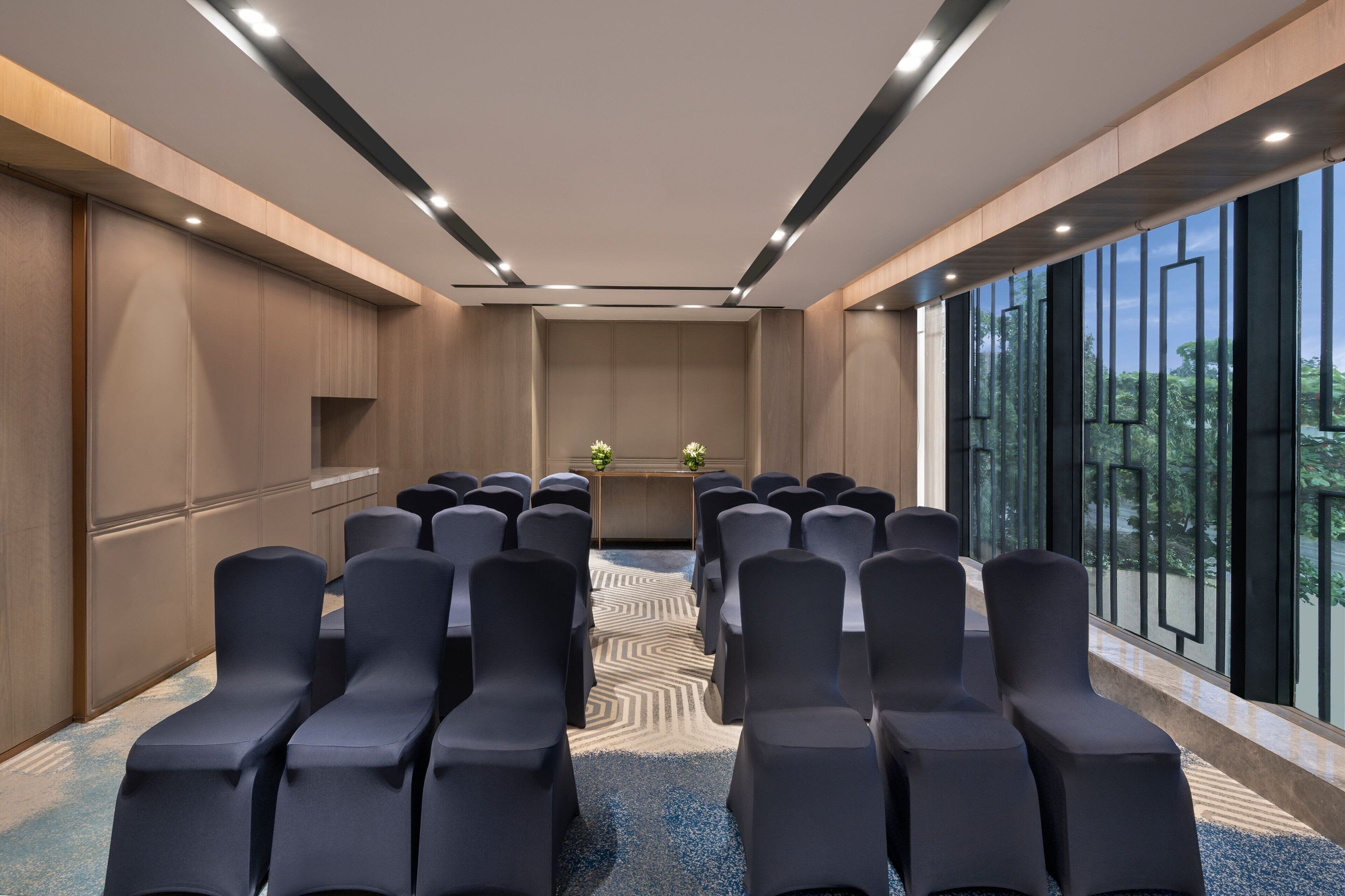 Un salón de conferencias con filas de sillas, un atril y un ventanal con vistas a árboles.