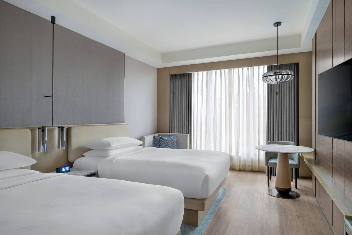 Een hotelkamer met twee bedden, een televisie, een klein tafeltje en een raam met gordijnen.