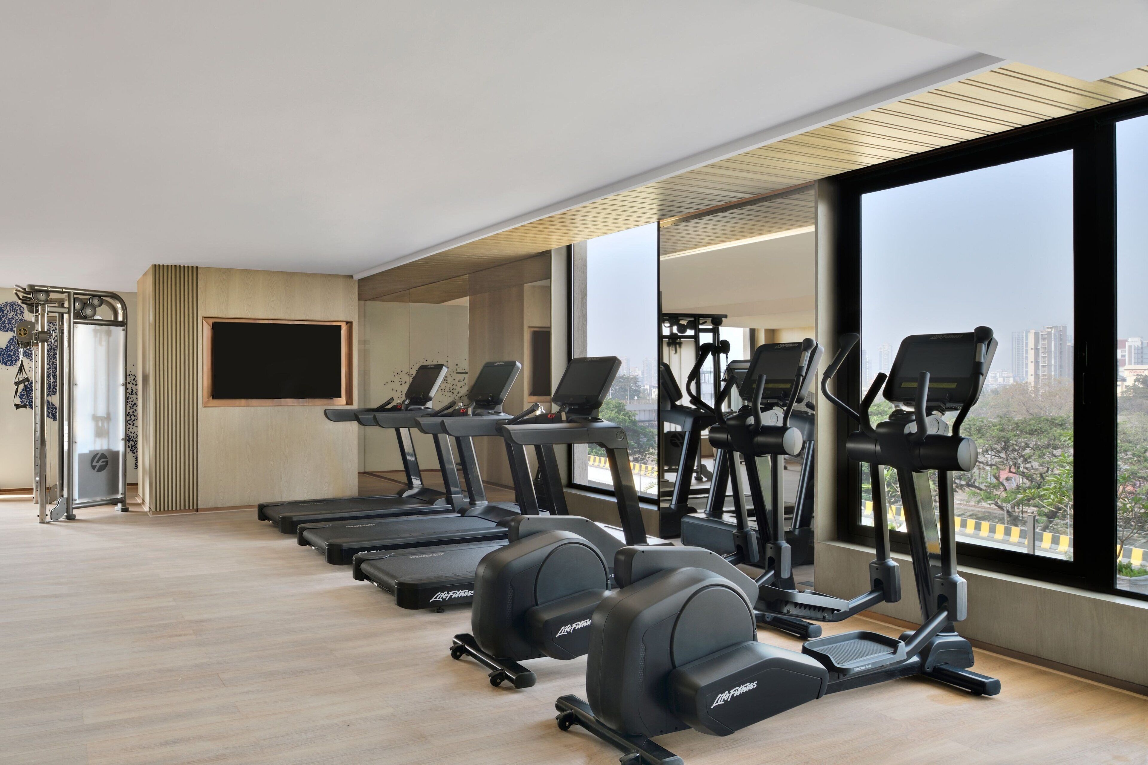 Un gimnasio con cintas de correr, elípticas y un amplio ventanal con vistas a la ciudad.