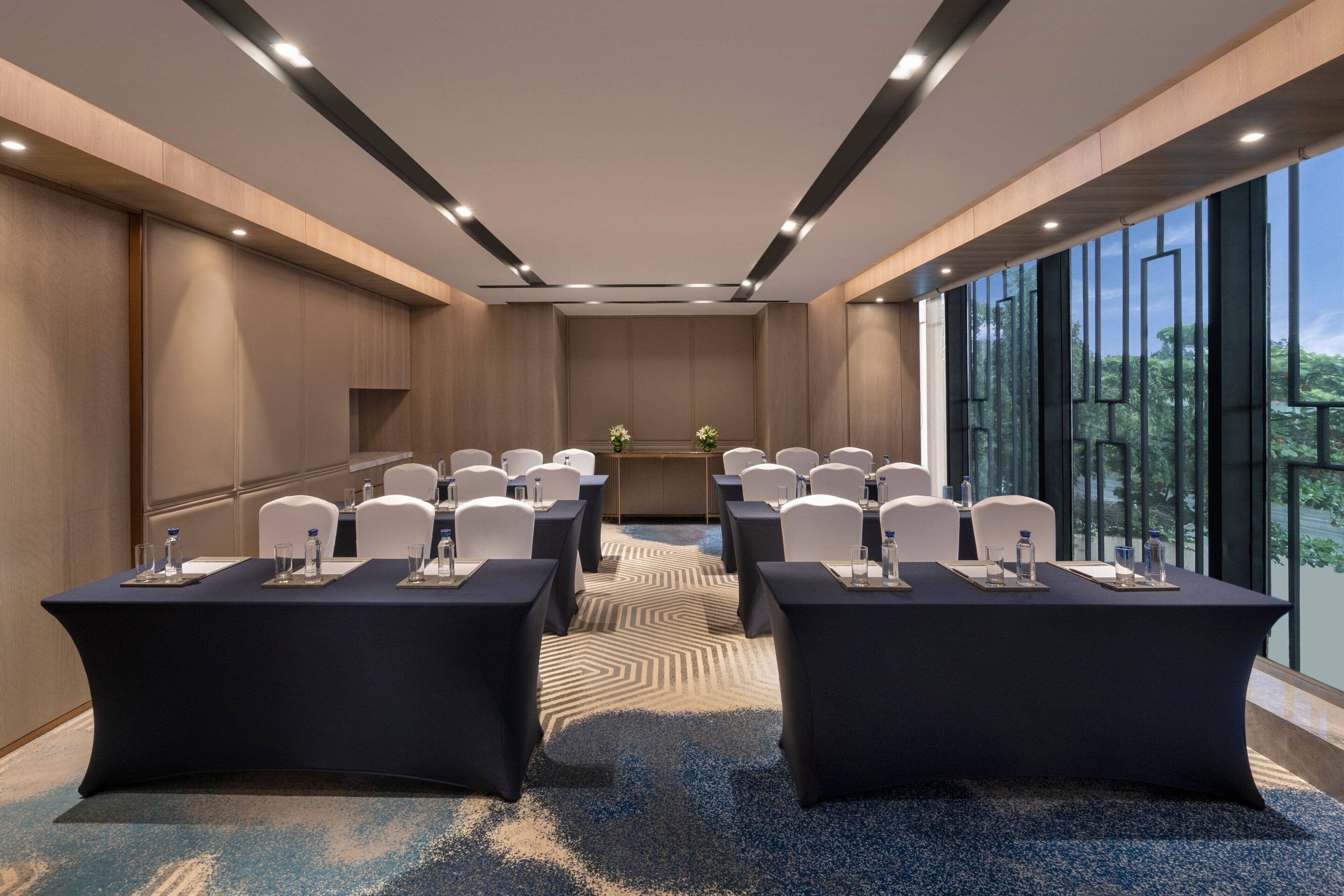 Une salle de conférence dotée d’une longue table, de chaises blanches et d’une grande fenêtre donnant sur un paysage verdoyant.