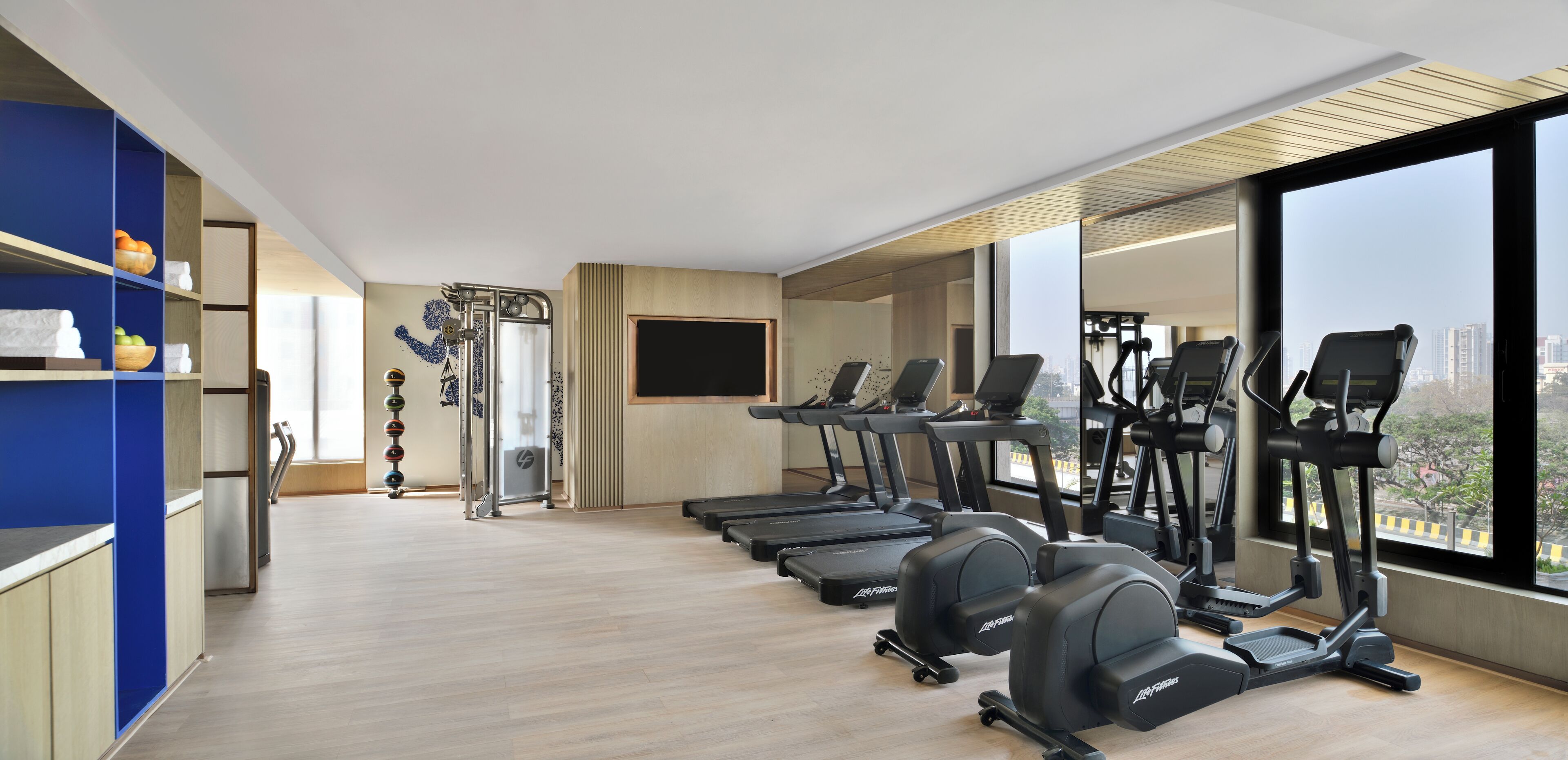Een moderne sportschool met loopbanden, elliptische trainers en een groot raam met uitzicht op de stad.