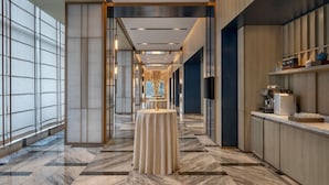 Un pasillo moderno de hotel con suelo de mármol, una mesa redonda y una máquina de café a la derecha.