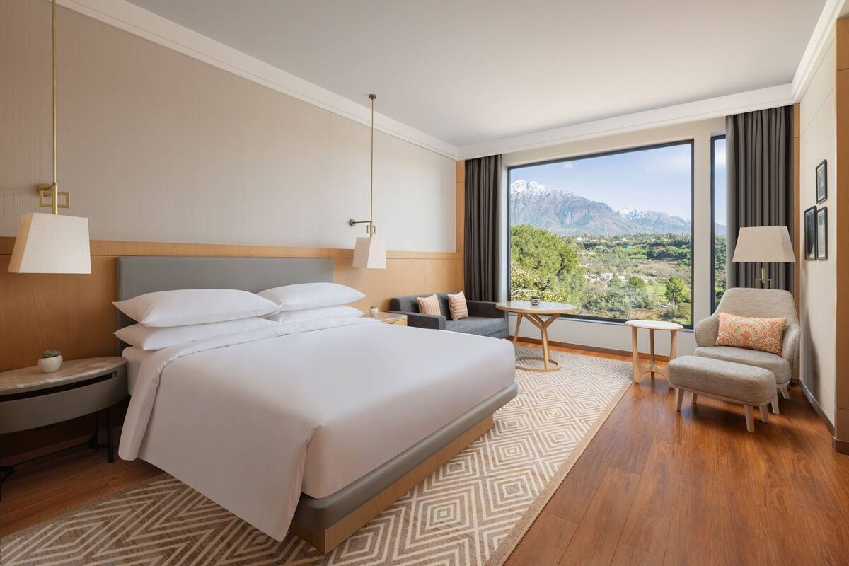 Habitación de hotel con una cama grande, un sofá, una mesita y vistas a un paisaje montañoso.