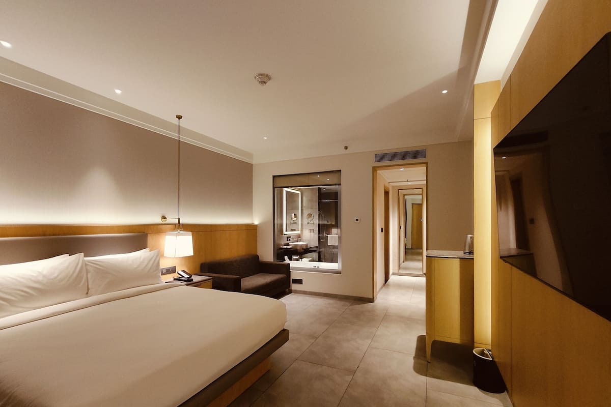 Una habitación de hotel con una cama grande, un escritorio, una silla, un espejo y un baño visible a través de una puerta abierta.