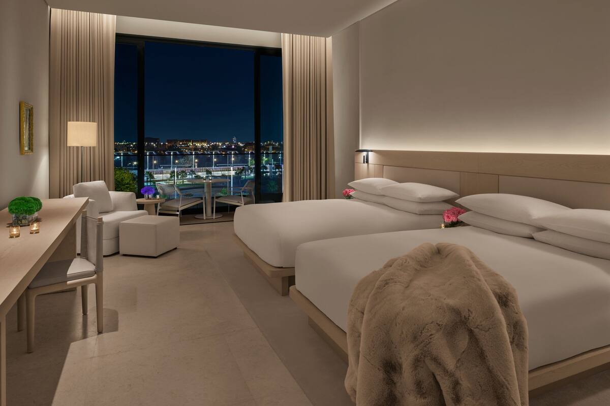 A modern hotel room with a large bed, a desk, and a balcony with a city view.