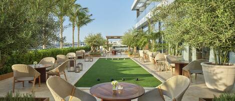 A rooftop lounge with a green lawn, wicker furniture, and a view of the sea.
