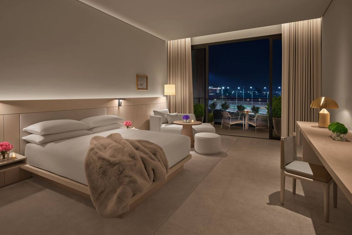 A modern hotel room with a large bed, a desk, a chair, and a balcony with a city view.