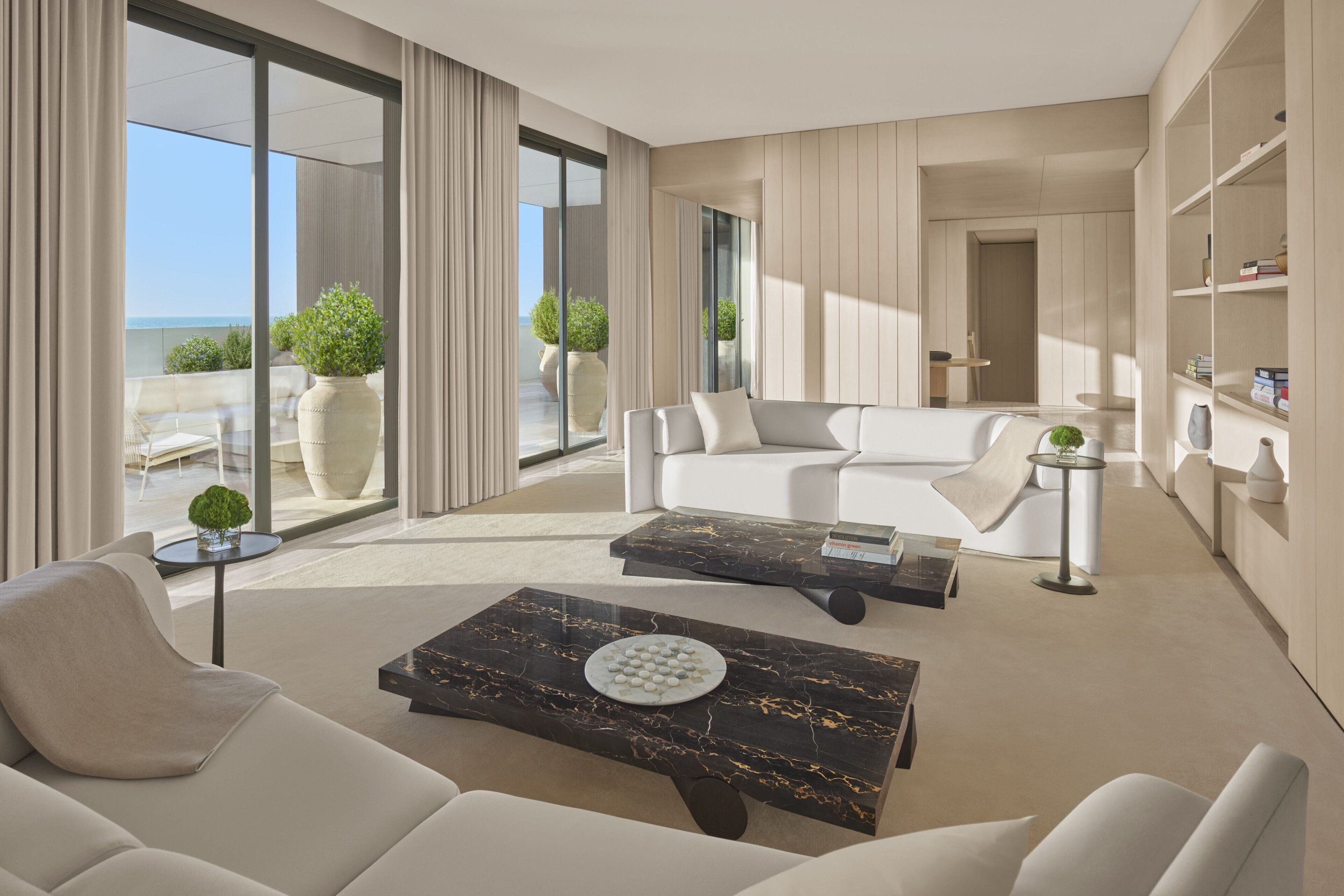 Una sala de estar moderna con un sofá, una mesa de centro y una estantería. Hay un ventanal con cortinas y vistas al exterior.