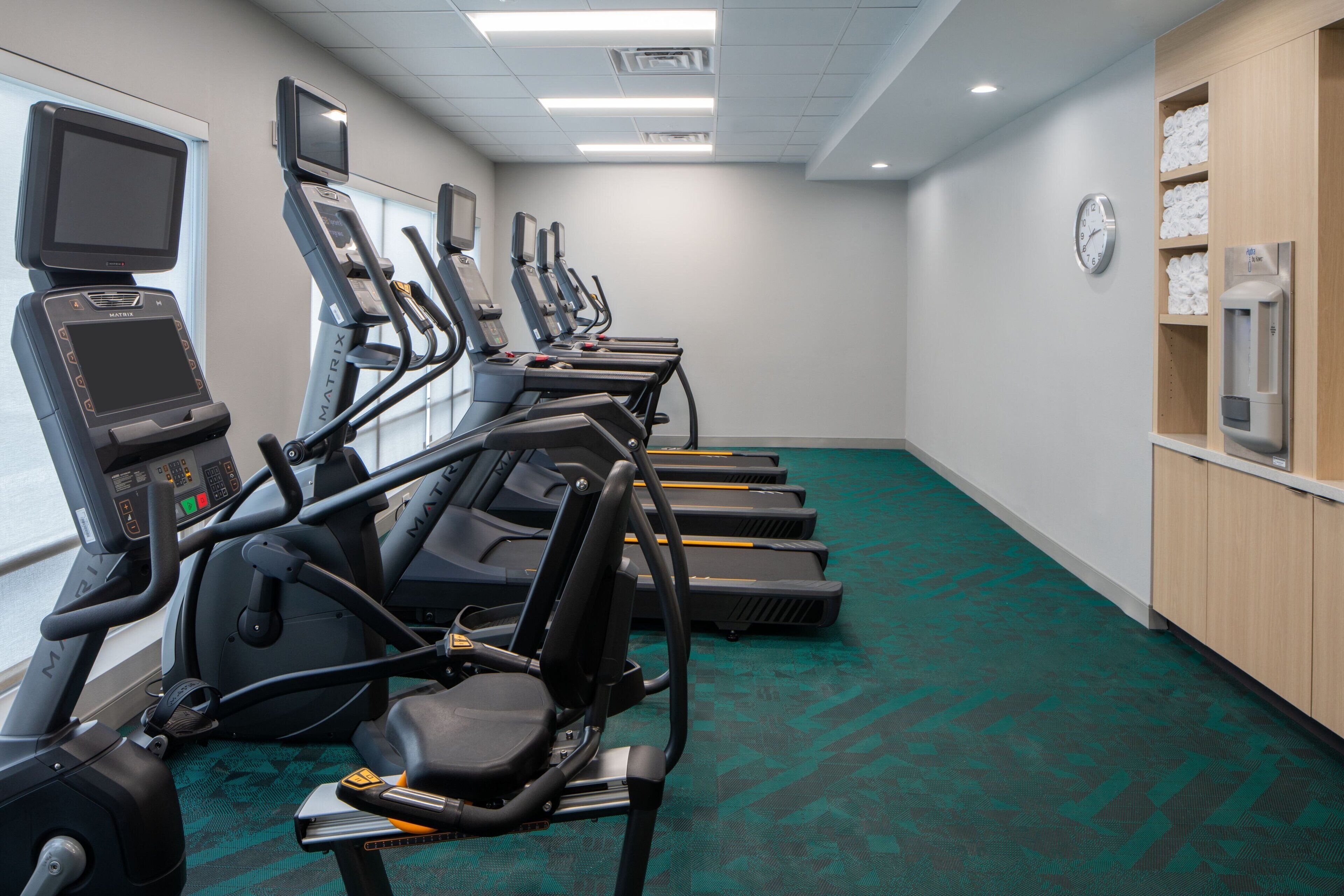 A fitness room with treadmills, exercise bikes, and a clock on the wall.