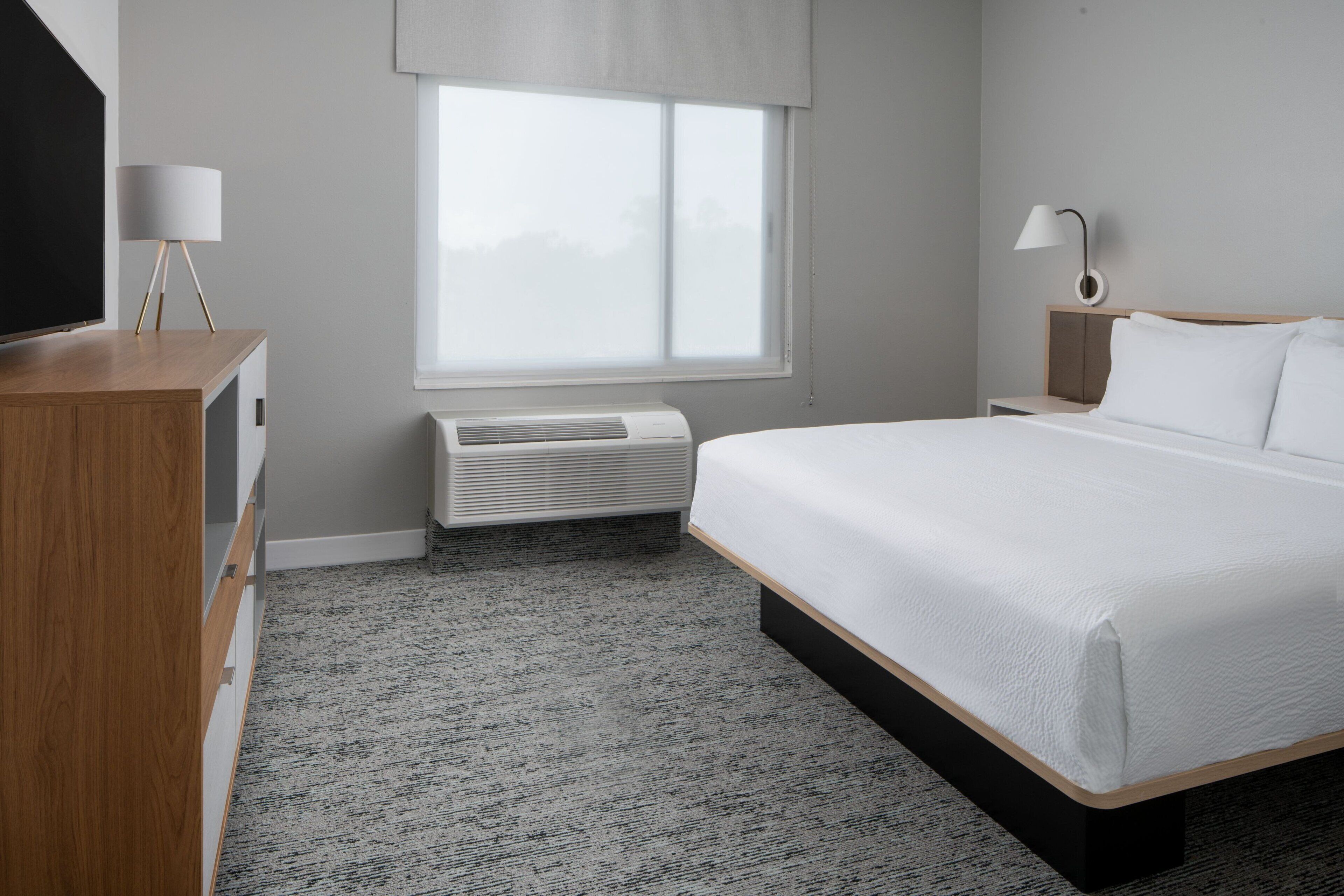 Habitación de hotel con una cama grande, televisión, escritorio, lámpara y ventana con persianas.