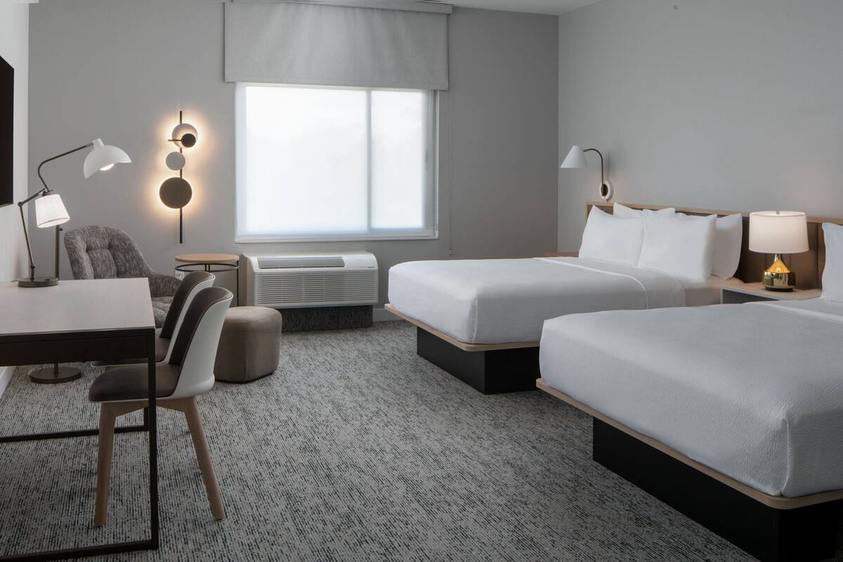 A hotel room with two beds, a desk, a chair, and a small table.
