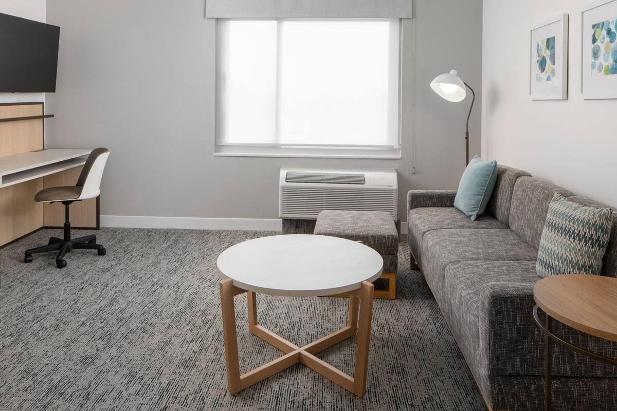 A modern room with a desk, chair, round table, sofa, and a standing lamp.