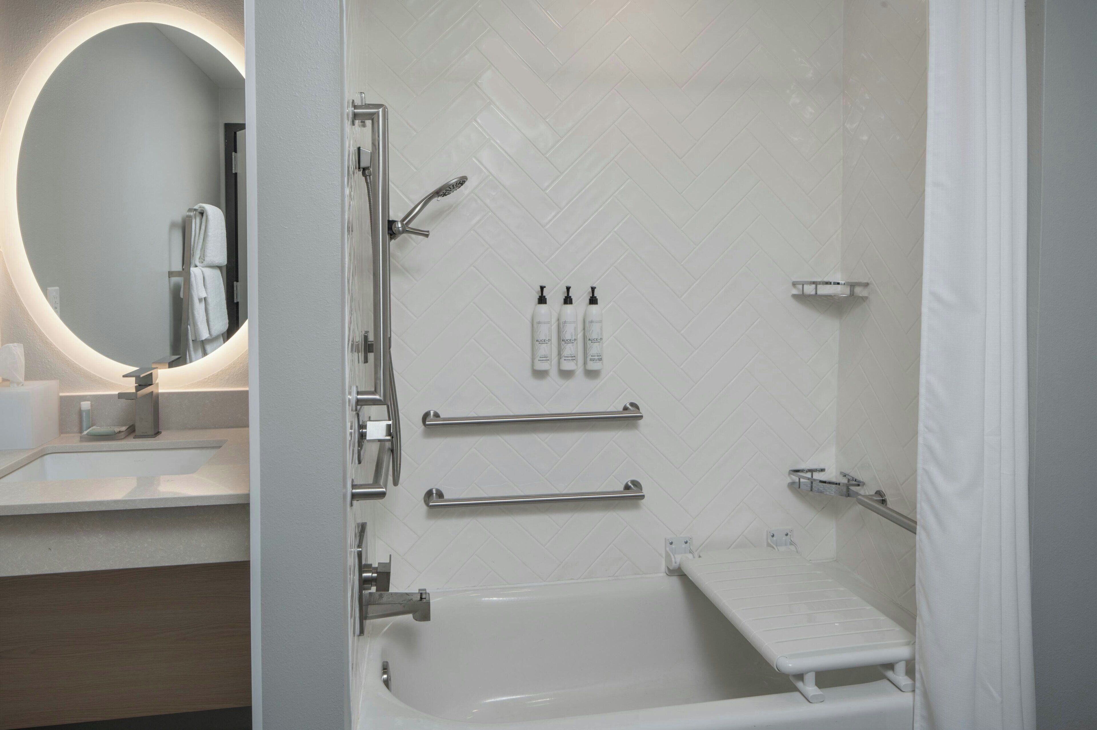 A modern bathroom with a white bathtub, a round mirror, and a shower area.