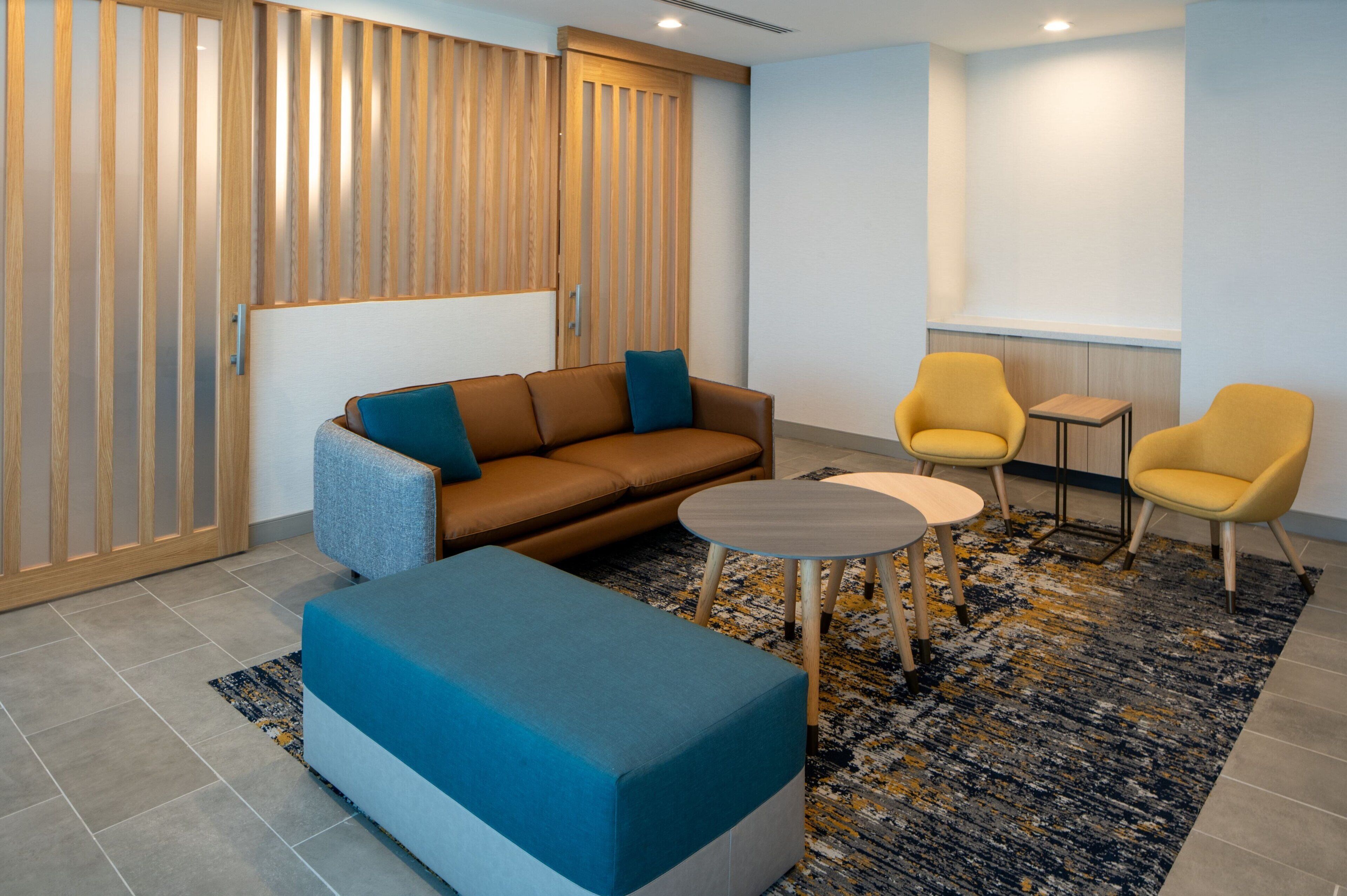 A modern lounge area with a sofa, two armchairs, a small table, and a patterned rug.