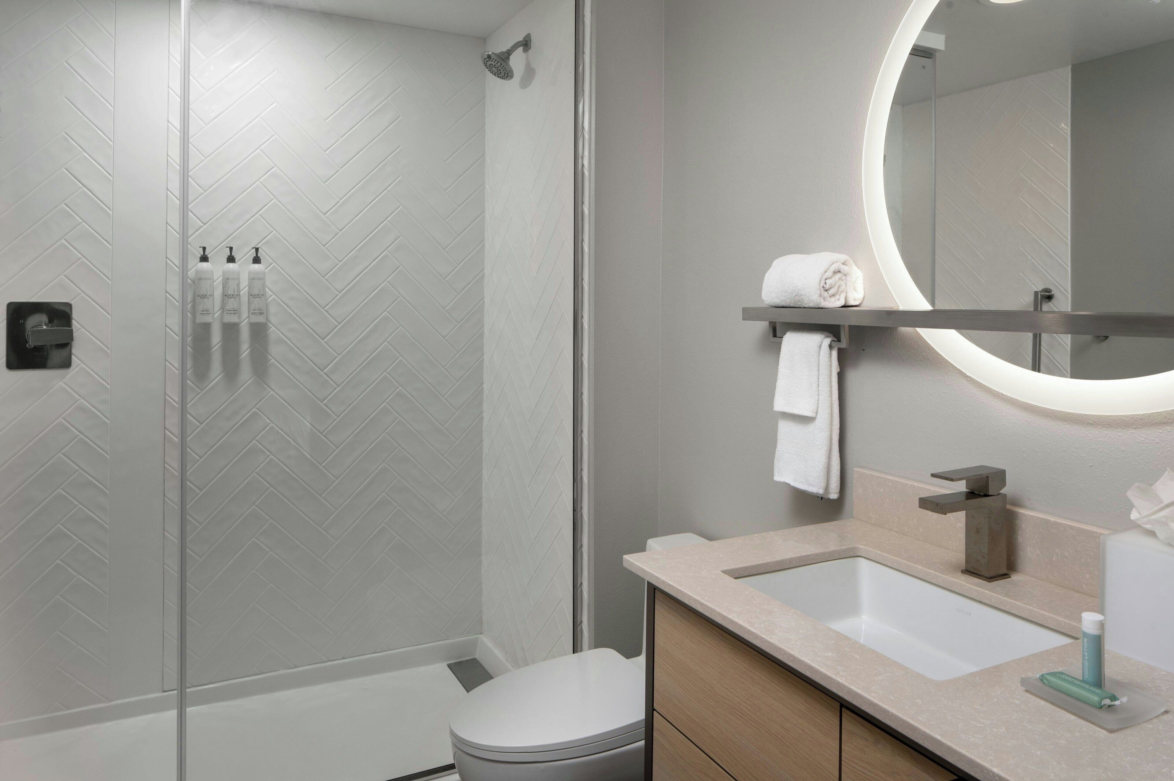 A modern bathroom with a shower, toilet, sink, and mirror.