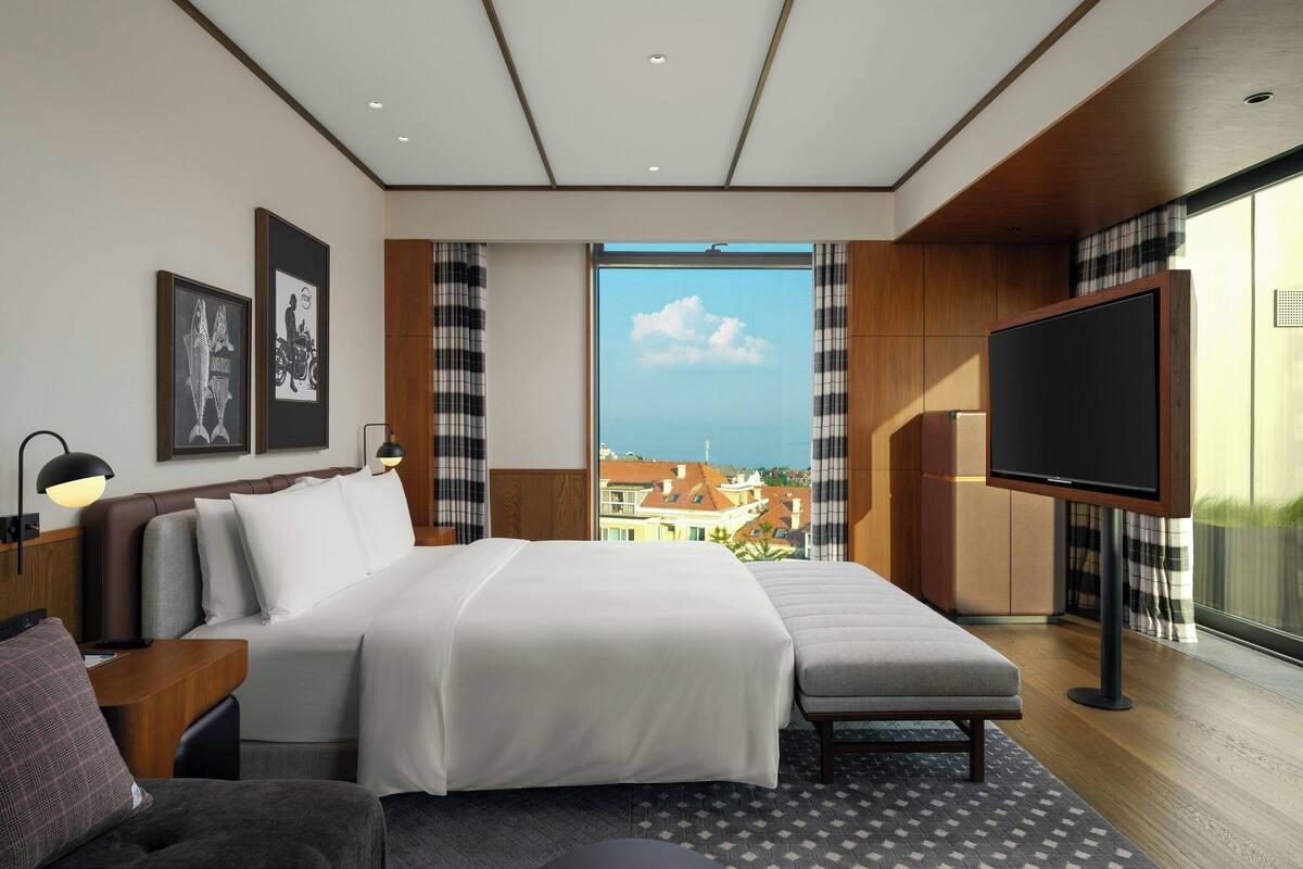 A modern hotel room with a large bed, a TV, and a view of the city.
