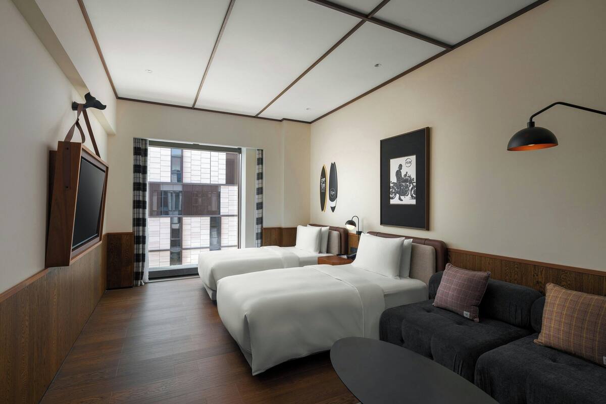A hotel room with two beds, a sofa, a desk, and a TV.