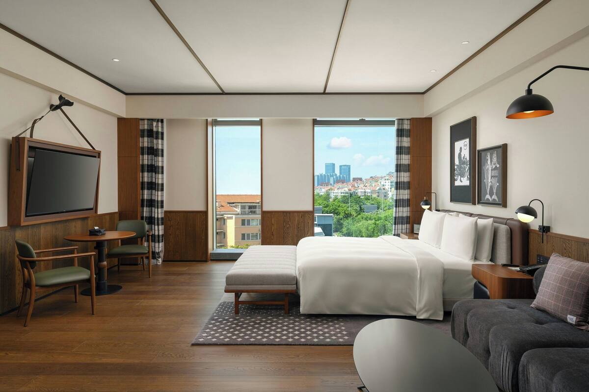 A modern hotel room with a large bed, a sofa, a desk, and a TV.