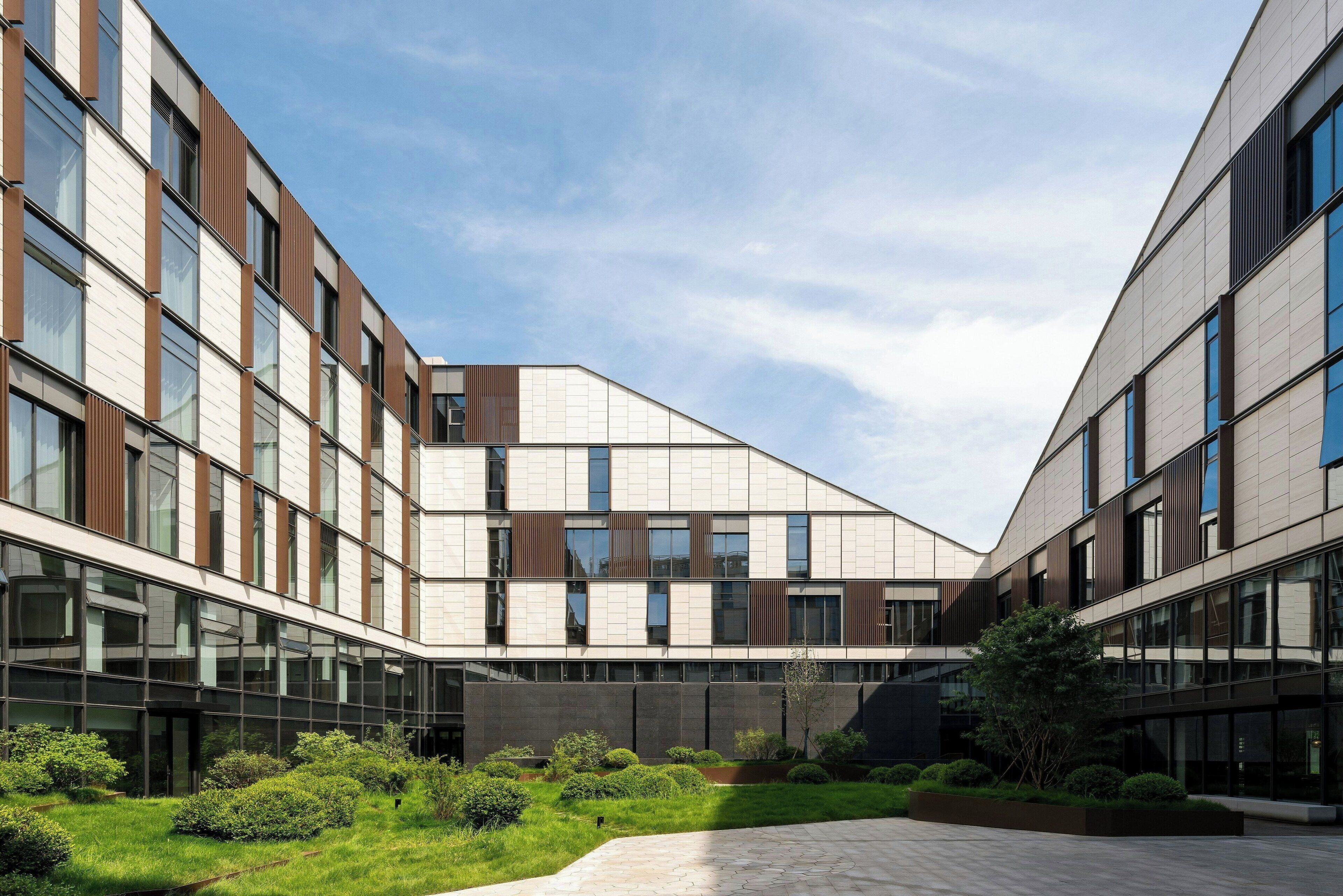 Een modern gebouw met een binnentuin, met een glazen gevel, een geometrisch dak en een aangelegde tuin.
