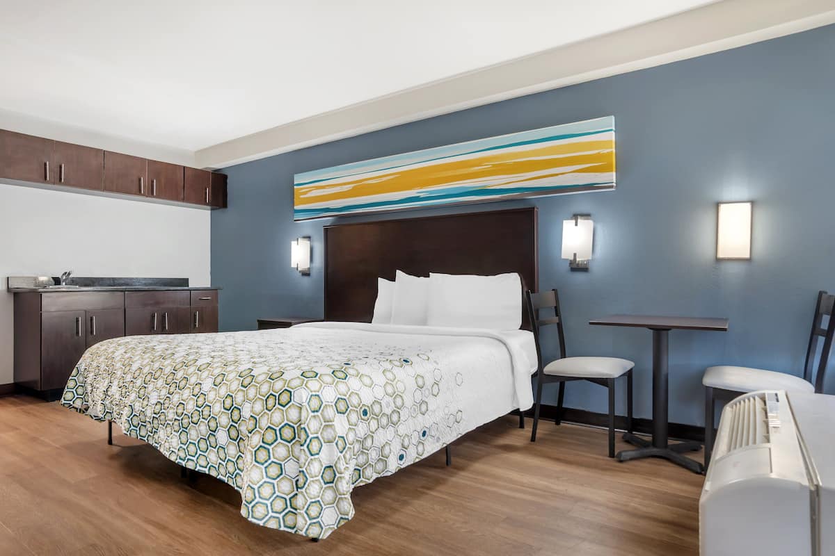 A hotel room with a bed, a desk, a chair, a small table, and a wall-mounted artwork.