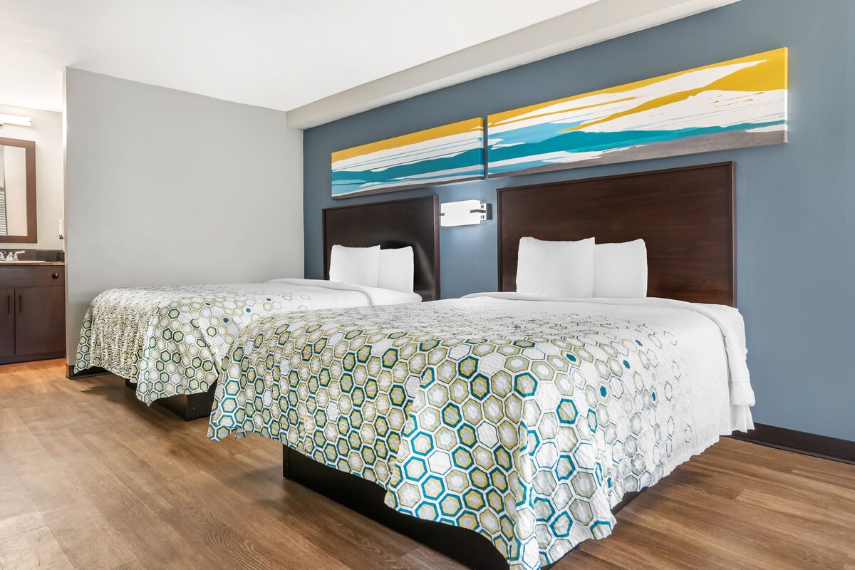 A hotel room with two beds, a large abstract painting on the wall, and a wooden floor.