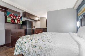 A hotel room with a bed, a TV mounted on the wall, a refrigerator, and wooden cabinets. - HomeTowne Studios by Red Roof Montgomery - Midtown (Montgomery)