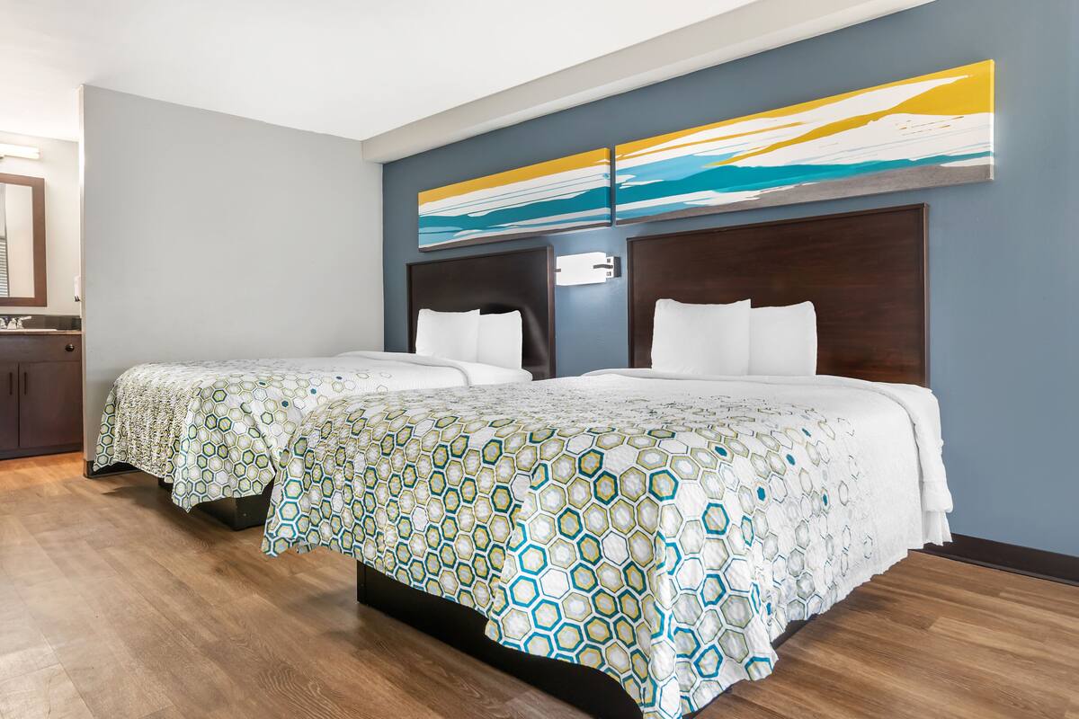 A hotel room with two beds, a large abstract painting on the wall, and a wooden floor.