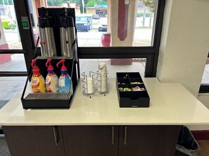Un comptoir équipé d’un espace pour préparer le café, de distributeurs de condiments et d’une poubelle.
