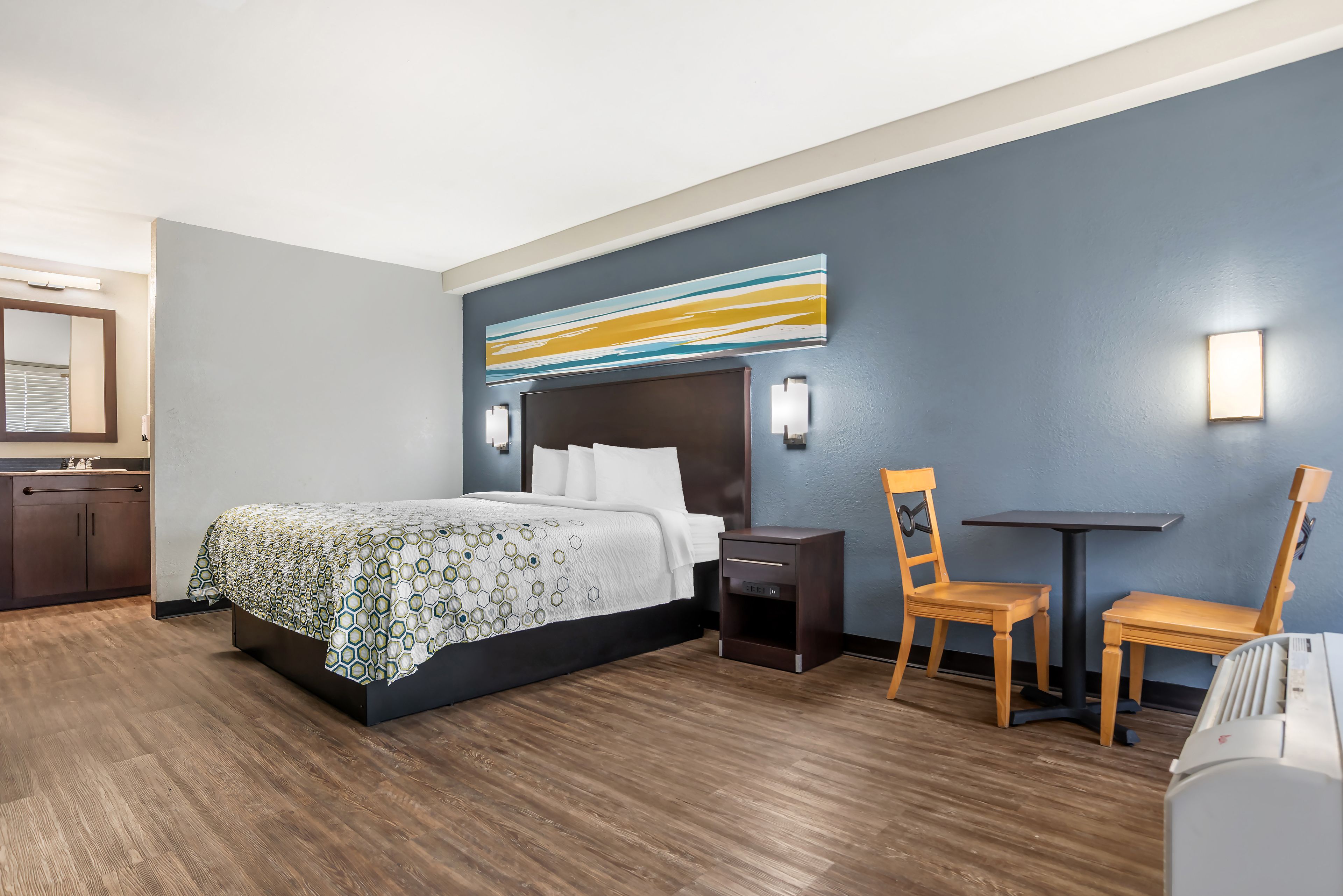 Une chambre d’hôtel comprenant un lit, une table de chevet, une chaise et une petite table avec une chaise.