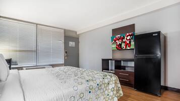 A hotel room with a bed, a refrigerator, a television, and a window with blinds.