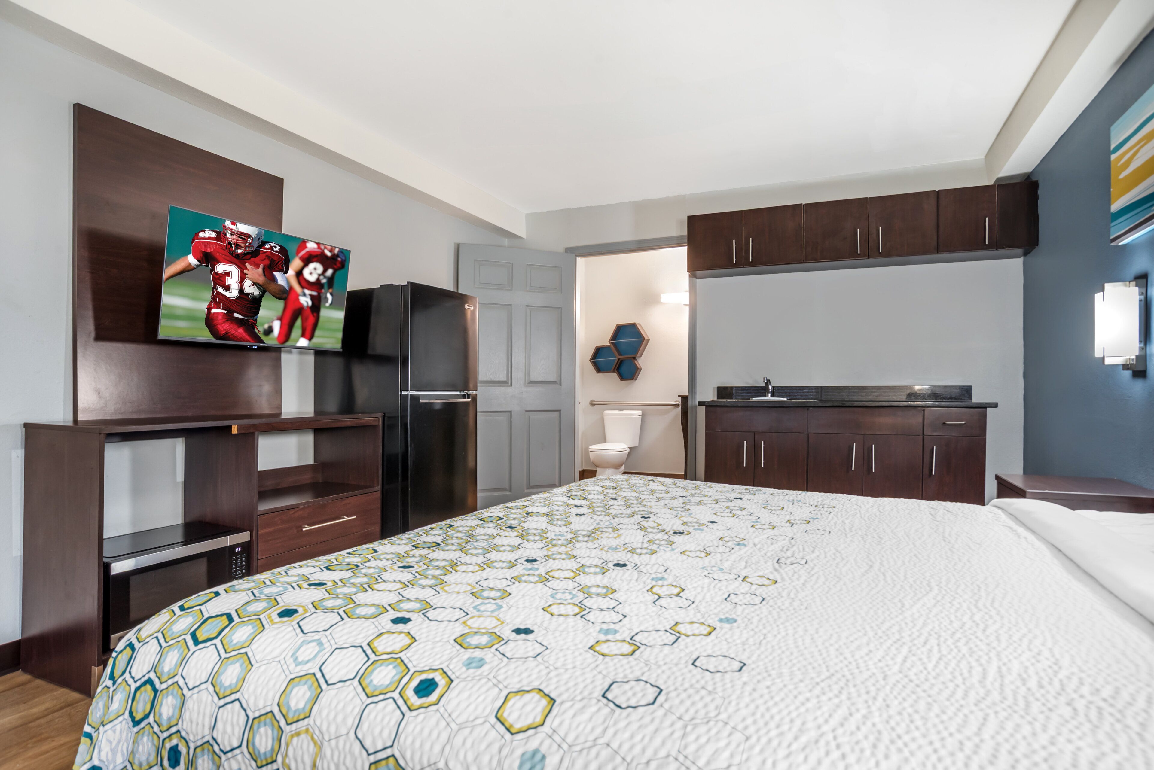 A hotel room with a bed, a TV mounted on the wall, a refrigerator, and a microwave.