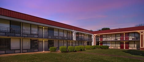 A two-story motel with a red roof, multiple balconies, and a grassy courtyard.