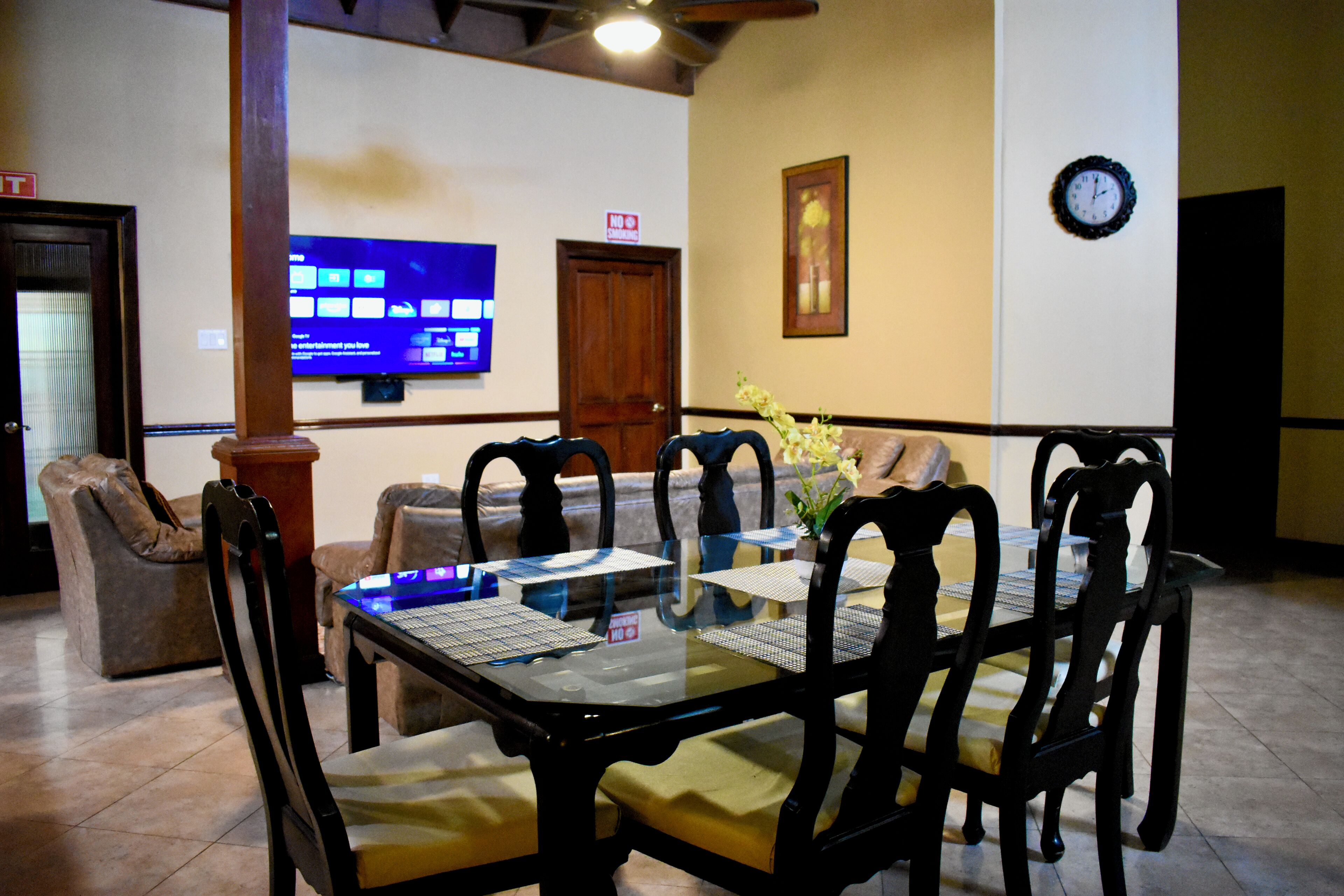 A dining area with a glass-top table, black chairs, and a floral centerpiece.