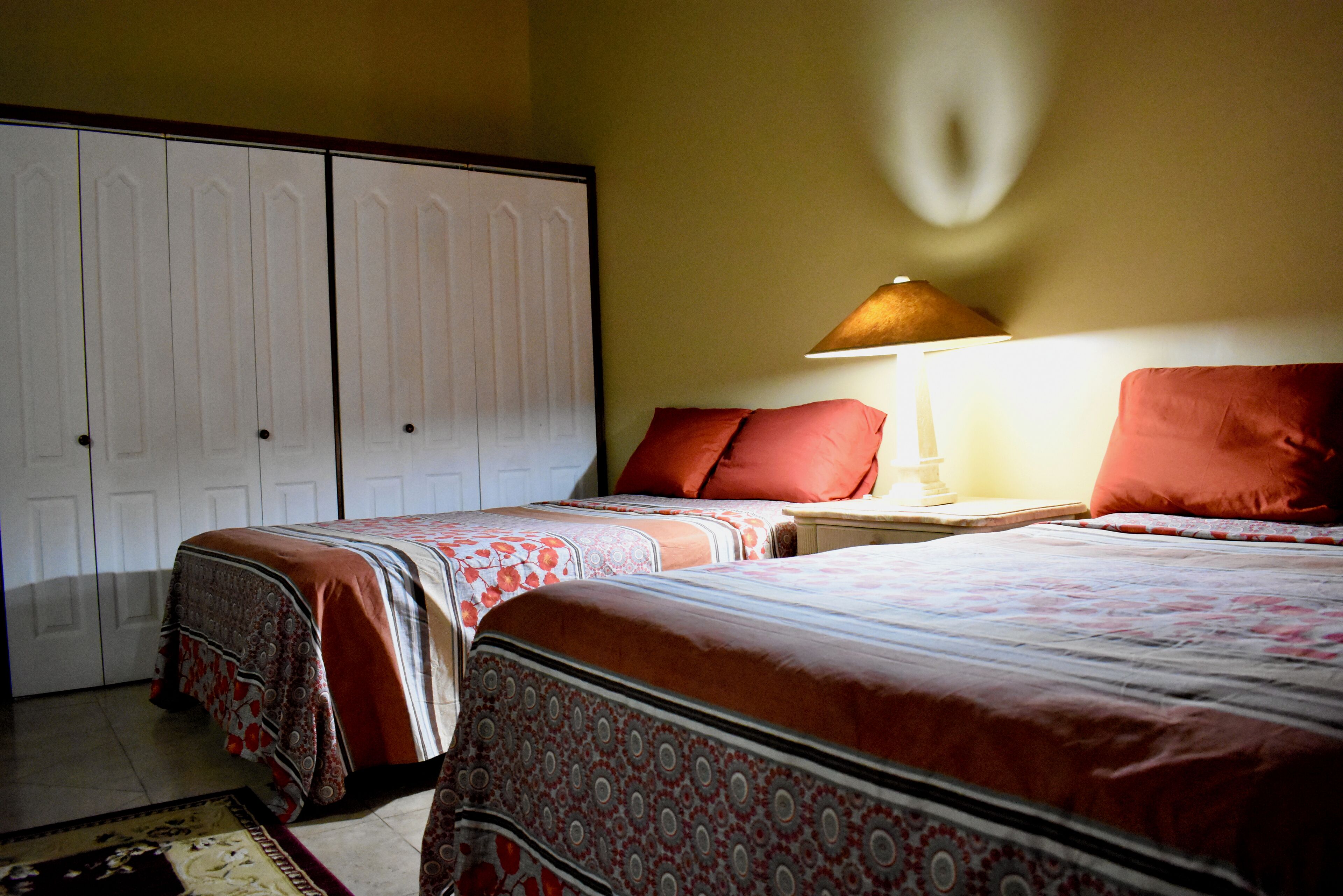A bedroom with two beds, a nightstand, a lamp, and a wardrobe.
