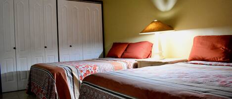 A bedroom with two beds, a nightstand, a lamp, and a wardrobe.