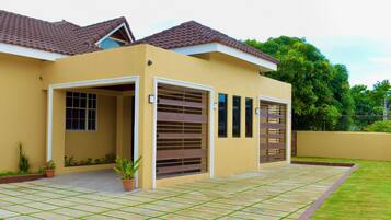 A modern house with a tiled roof, a garage with a brown gate, and a paved driveway with potted plants.