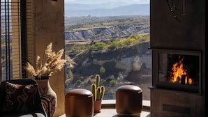 A living room with a fireplace, a large window with a view of a mountainous landscape, and a cactus plant. - Very Peri Cappadocia - The Lifestyle Luxury Design Hotel  (Nevsehir)