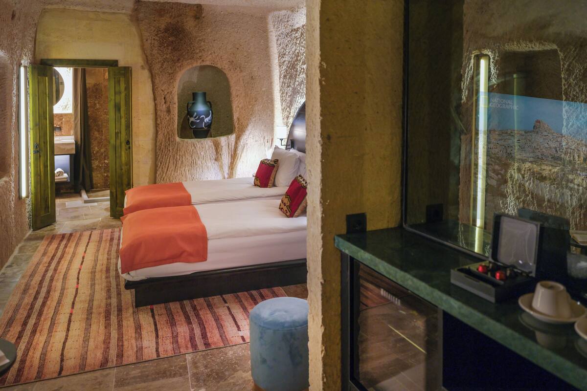 A room with a bed, a small table, a mirror, and a stone wall.