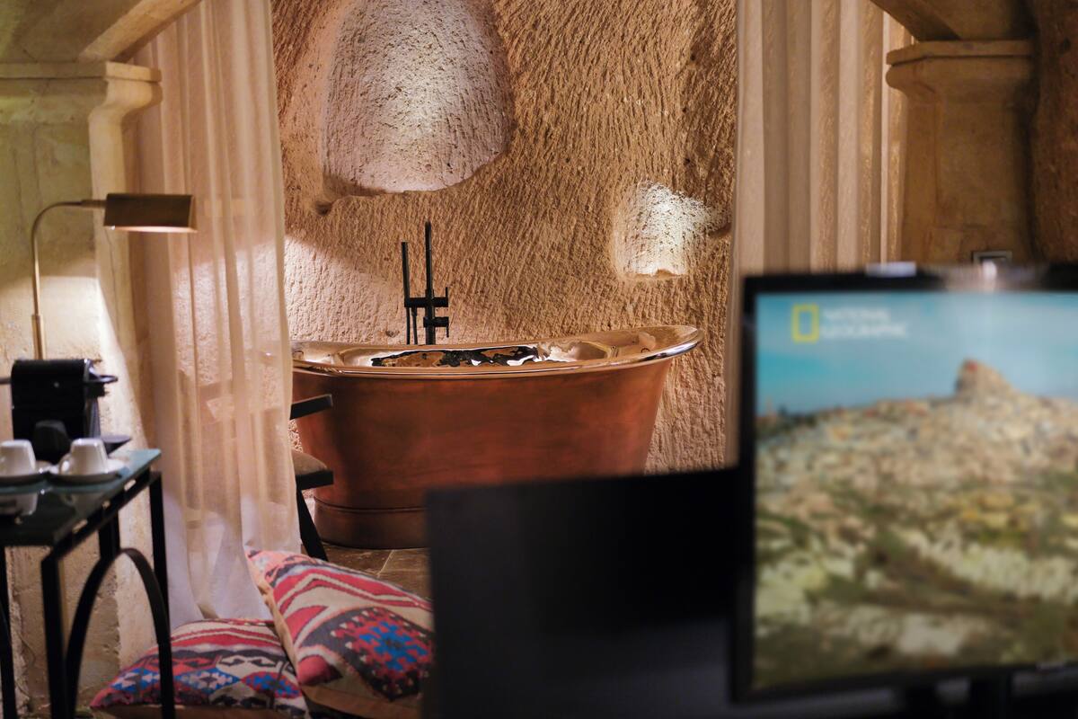 A cozy room with a large copper bathtub, a flat-screen TV, and a lamp.