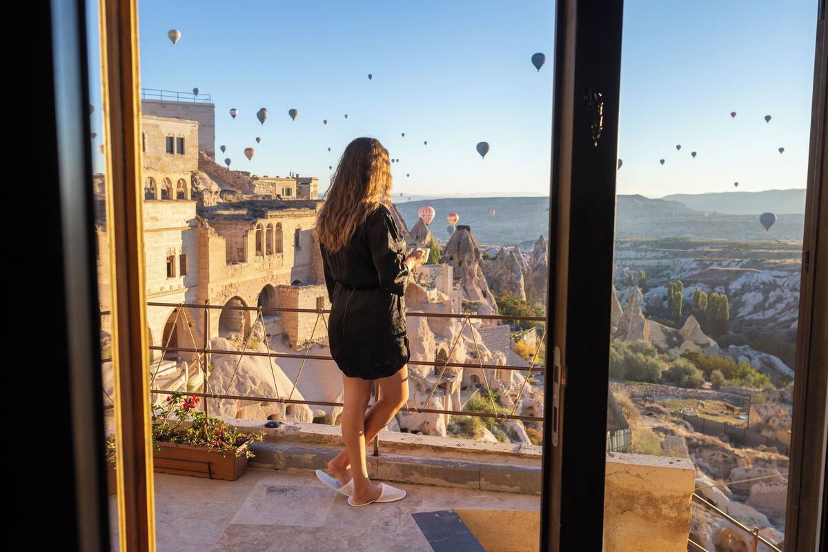 A person standing by a glass door overlooking a cityscape with historic buildings and a view of the sea.
