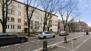 Katu, jonka varrella on parkkeerattuja autoja, puita ja korkeita rakennuksia.