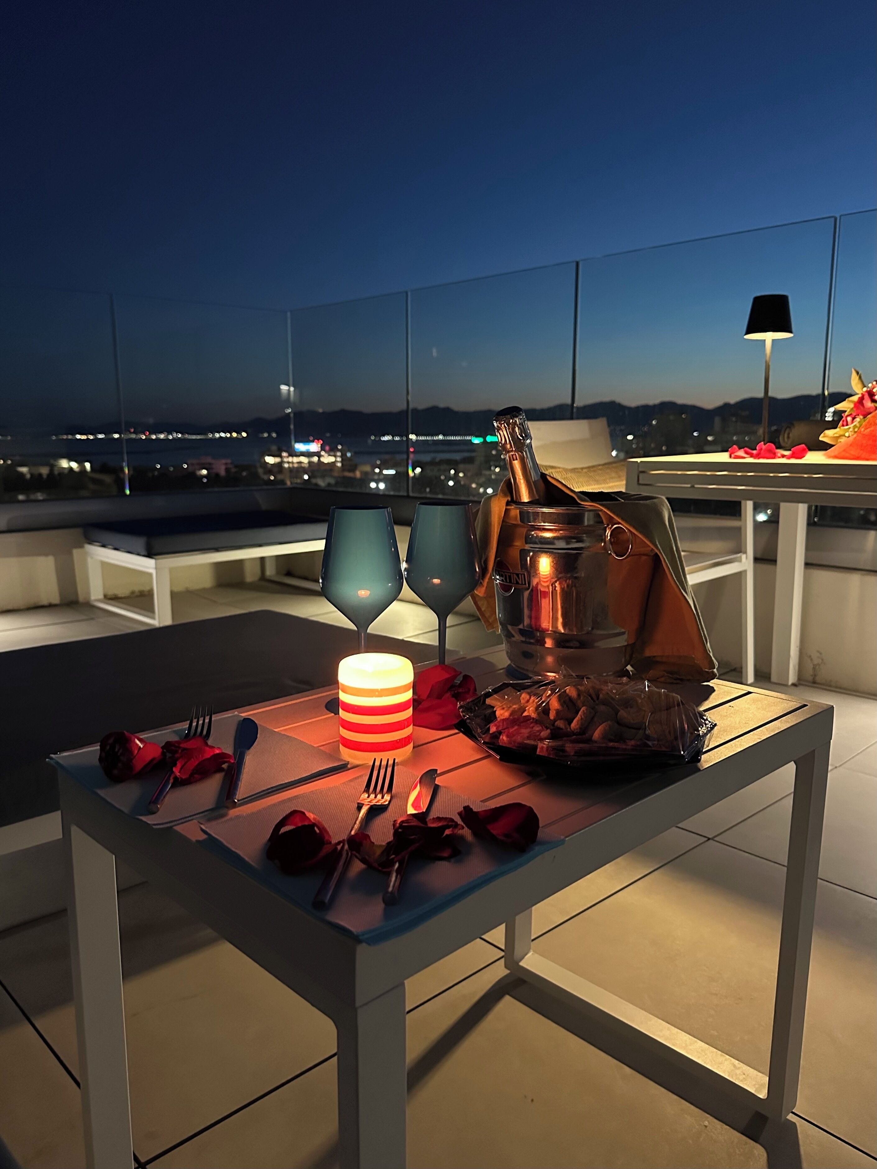 Um espaço de refeições no terraço com mesa, cadeiras, uma garrafa de champanhe e uma vela.