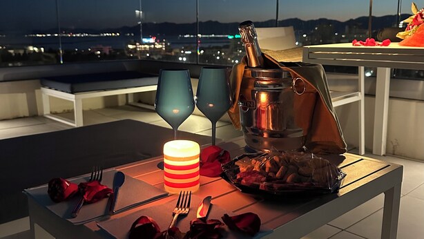 Um espaço de refeições no terraço com mesa, cadeiras, uma garrafa de champanhe e uma vela.