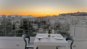 Un balcón con una mesa para dos, con vistas a un paisaje urbano al atardecer.