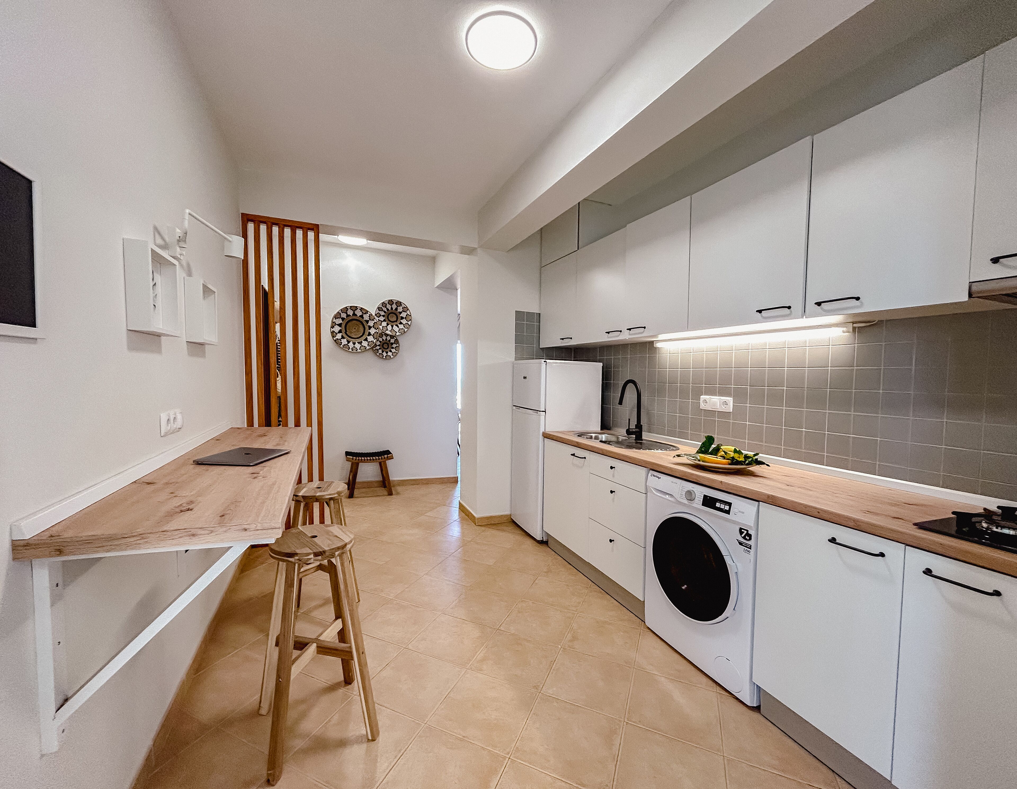 Una cocina moderna con encimera de madera, armarios blancos, una lavadora y una zona de comedor con taburetes.