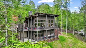 A multi-story wooden cabin with balconies, surrounded by lush greenery and trees. - Brand NEW Luxury Chalet! Summer Sale! (Epworth)