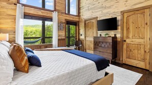 A wooden cabin bedroom with a large bed, a TV mounted on the wall, and a view of the outdoors. - Brand NEW Luxury Chalet! Summer Sale! (Epworth)
