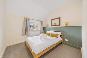 Een slaapkamer met een houten bed, een raam met gordijnen, een spiegel en een bedlamp.