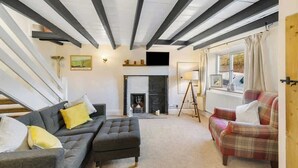 A living room with a fireplace, a sofa, an ottoman, and a plaid armchair. - Cosy Country Cottage Sleeps 4 (Kirkbymoorside)
