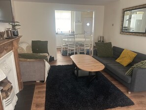A living room with a sofa, a coffee table, and a dining area with chairs and a table. - Manchester, Levenshulme, Entire House, Sleeps 7max (Manchester)